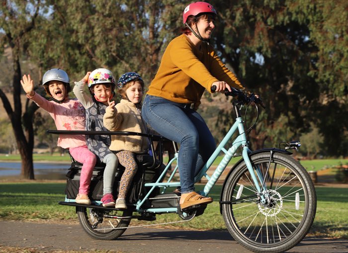 3 kids on the back of a cargo bike with an adult driving it