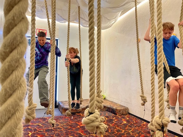 two adults and a child on ropes where the floor is lava